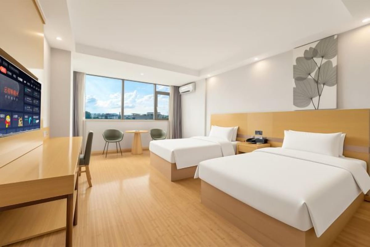 A hotel room with two beds, a desk, a chair, a small table, and a view of the city.