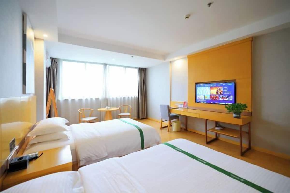 A hotel room with two beds, a desk, a television, and a window with curtains.