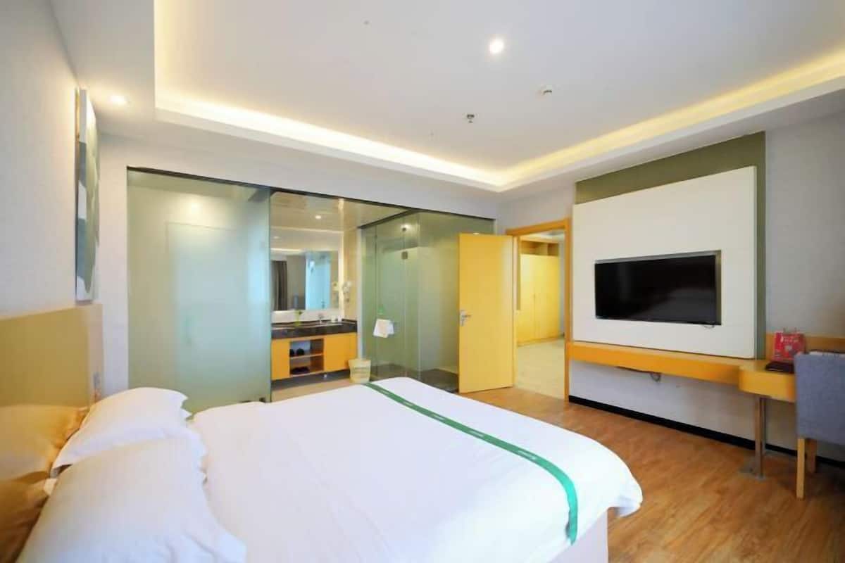 A hotel room with a bed, a TV, a mirror, and a bathroom visible through a glass door.