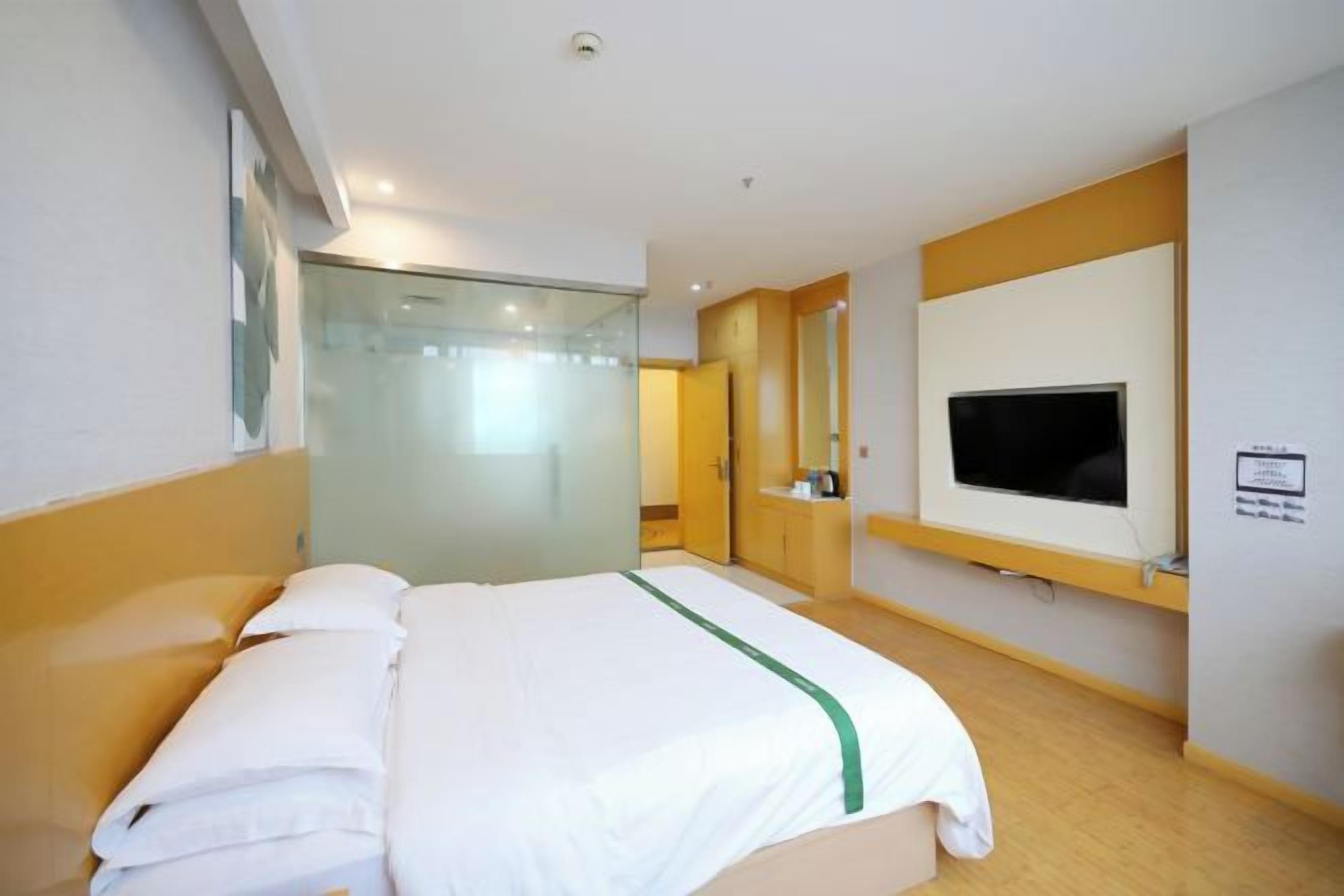 A hotel room with a bed, a TV, a mirror, and a glass partition.