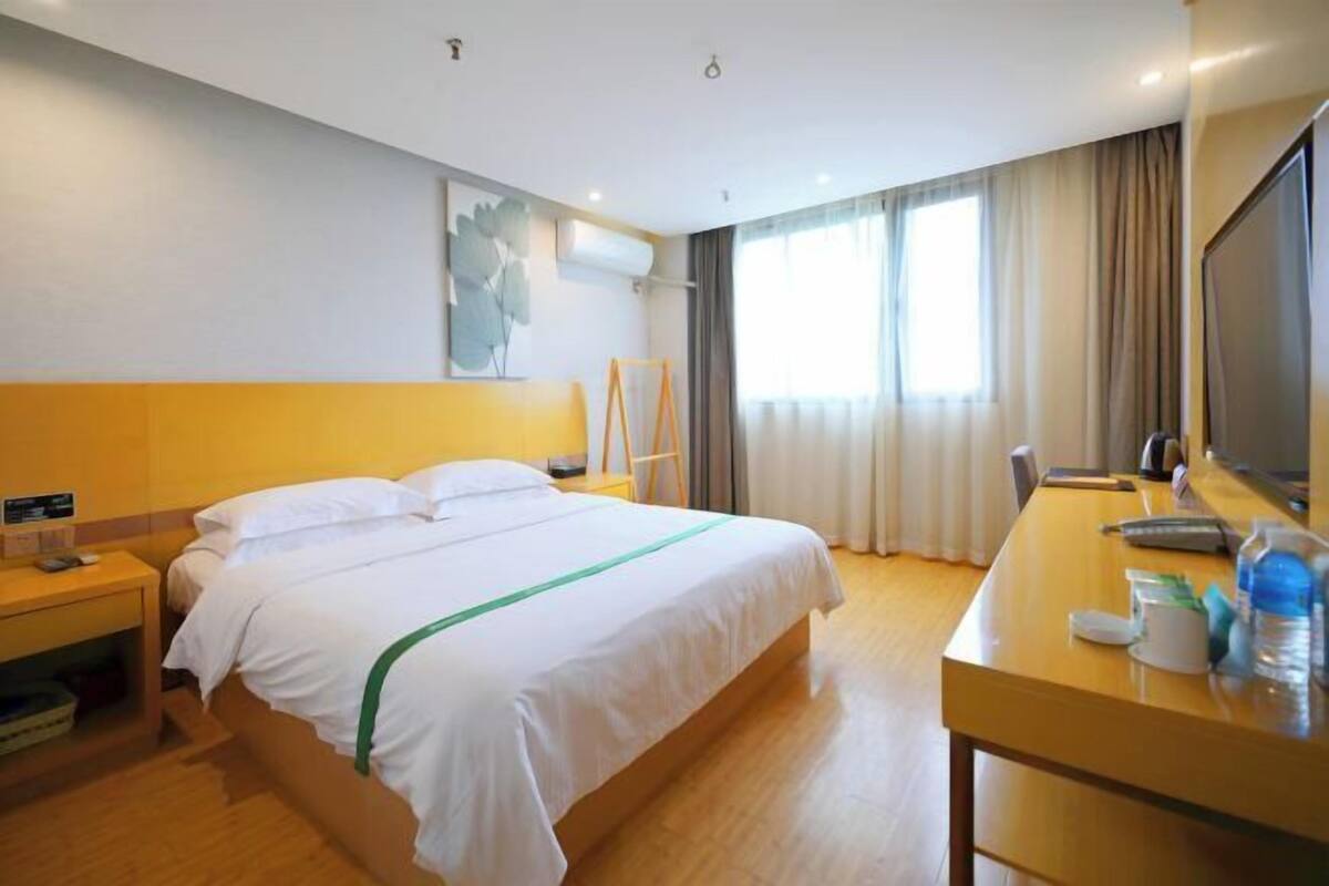 A hotel room with a bed, a desk, a chair, a TV, and a window with curtains.