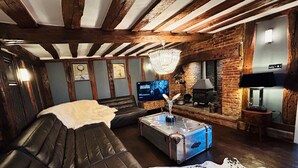 Ein gemütliches Wohnzimmer mit freiliegenden Holzbalken, einem Ledersofa, einem Glastisch und einem Kamin.