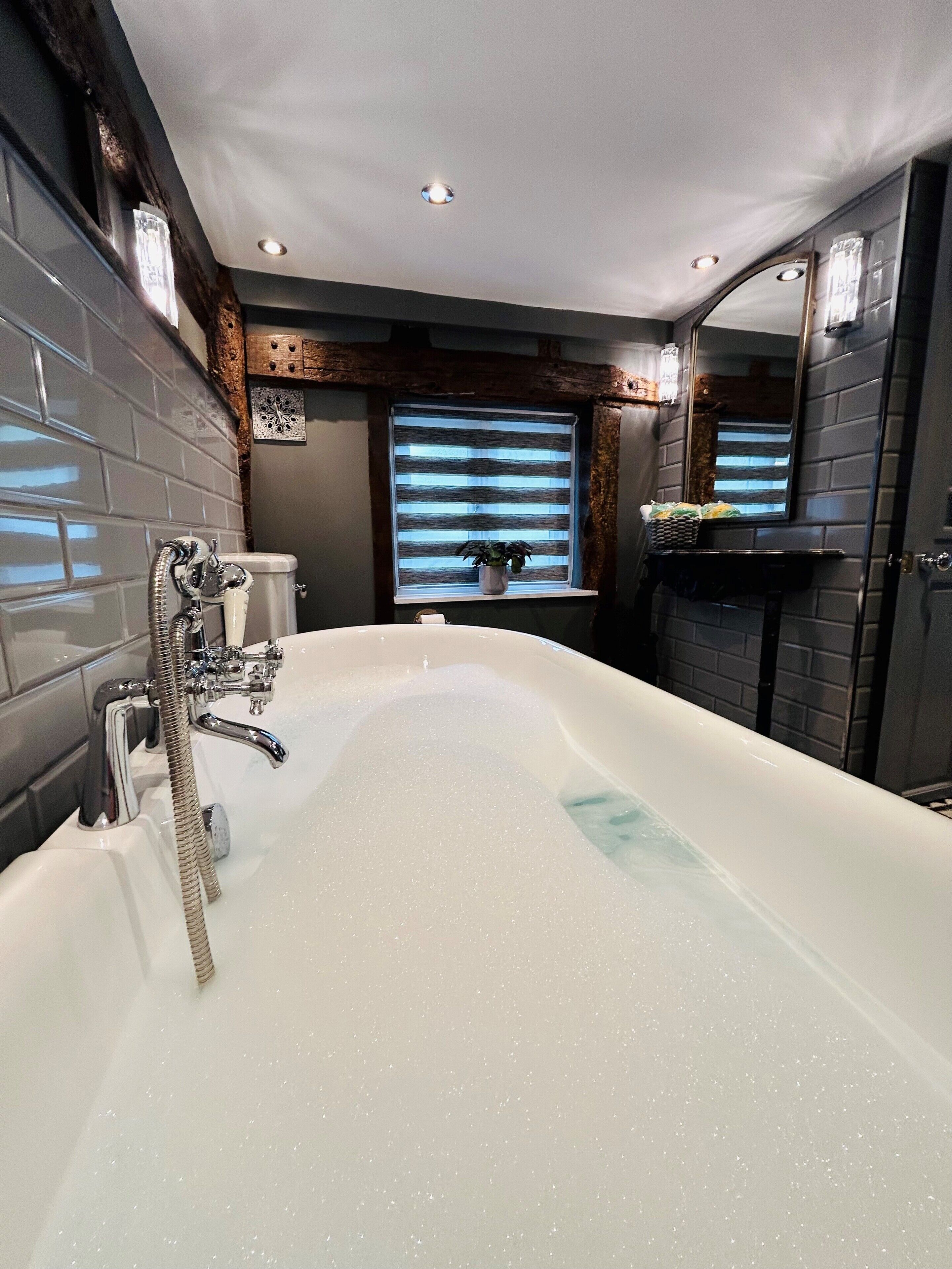 A modern bathroom with a large bathtub, a toilet, and a window with blinds.