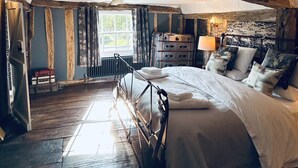 Ein rustikales Schlafzimmer mit Holzbalkendecke, einem großen Bett, einem Schminktisch und einem Fenster.