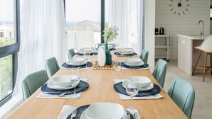 A dining area with a wooden table set for six, surrounded by chairs, with a view of the sea through large windows. - Villa Coastal Bliss with private pool & sea view at Jan Thiel (Jan Thiel)