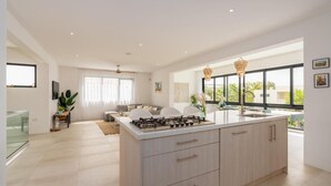Une cuisine moderne dotée d’un grand îlot central, d’un coin repas avec un canapé et des chaises, et de grandes fenêtres offrant une vue dégagée.