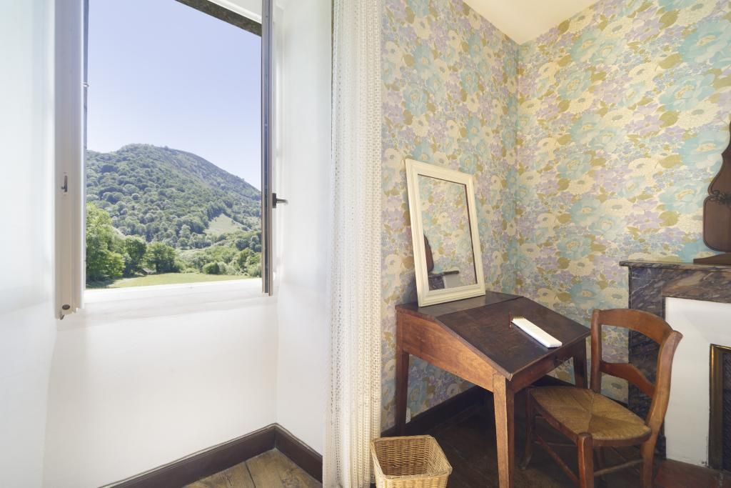 Una stanza con vista su una montagna, una scrivania in legno con una sedia e un quadro appeso al muro.