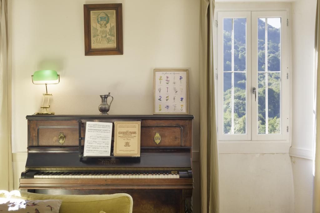 Un piano con partituras, un cuadro enmarco y una ventana con vistas a la vegetación.