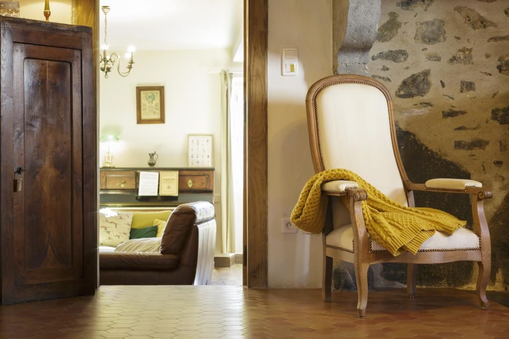 A room with a wooden door, a brown leather sofa, a white armchair with a yellow throw, and a tiled floor.