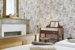 Une chambre à coucher avec un lit en bois, un petit bureau en bois doté d’un miroir, une cheminée et un papier peint à motifs floraux.