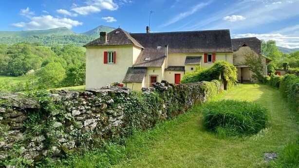 Une maison traditionnelle avec un mur en pierre et une cour gazonnée.