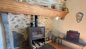 Un mur de pierres avec une cheminée, une étagère en bois au-dessus et un banc avec une pancarte.