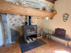 Un mur de pierres avec une cheminée, une étagère en bois au-dessus et un banc avec une pancarte.