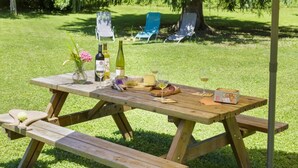 Juego de mesa de picnic de madera al aire libre con una botella de vino, copas, queso y un bol de fruta.