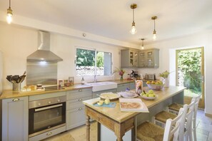A kitchen with a built-in oven, a sink, and a dining area with chairs. - Chez Jeanne, a charming farmhouse for 11 people with a spectacular view of the Pyrenees (ISSOR)
