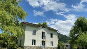 Une maison à deux étages, avec des fondations en pierre, un balcon et une pelouse bien entretenue.