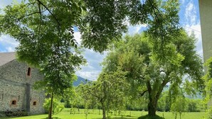 Un bâtiment en pierre avec une table de pique-nique, situé dans un espace verdoyant avec des arbres.