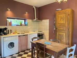 A compact kitchen with a washing machine, a sink, and a wooden dining table. - At Sylvain's: a trip down memory lane amid a large garden, a piano, a river, and the Pyrenees (ISSOR)