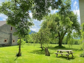 A stone building with a picnic table in a grassy area with trees. - At Sylvain's: a trip down memory lane amid a large garden, a piano, a river, and the Pyrenees (ISSOR)