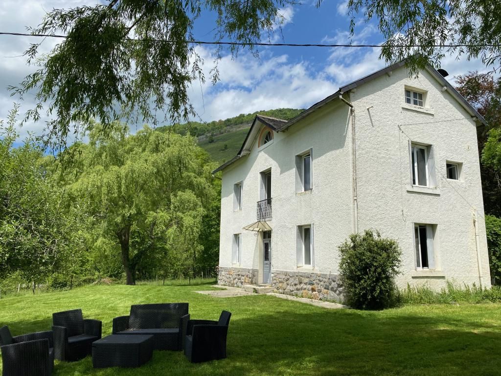 A two-story house with a stone foundation, a balcony, and a well-maintained lawn with outdoor furniture.