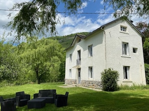 A two-story house with a stone foundation, a balcony, and a well-maintained lawn with outdoor furniture.