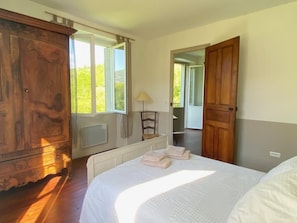 A bedroom with a large bed, wooden wardrobe, and a window with a view of greenery. - At Sylvain's: a trip down memory lane amid a large garden, a piano, a river, and the Pyrenees (ISSOR)