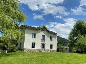 A two-story house with a stone foundation, a balcony, and a well-maintained lawn.