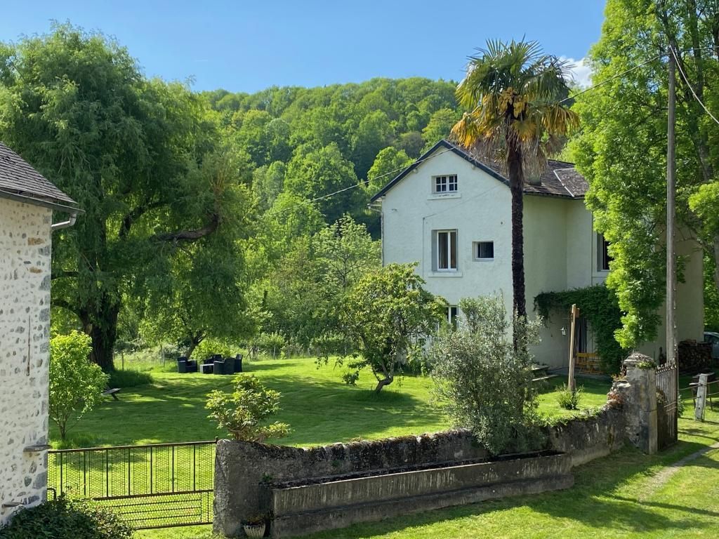 A white house with a sloped roof, surrounded by lush greenery and a well-maintained lawn.