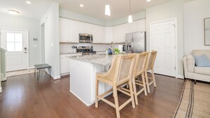 Een moderne keuken met witte kasten, roestvrijstalen apparatuur en een centraal keukenblok met barstoelen.
