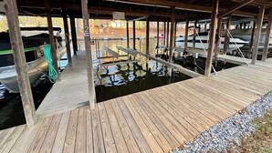 Een overdekt steigergedeelte met houten looppaden over het water, boten afgemeerd, en een groene slang aan de linkerkant.
