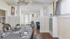 A dining area with a long table set for six, a chandelier, and a view of the dining room through a glass door. - Sleeps 12 • Budget-Friendly Downtown Birmingham Crew House (Birmingham)