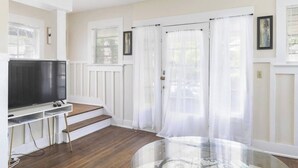 A living room with a flat-screen TV on a white stand, wooden flooring, and white curtains on the windows. - Sleeps 12 • Budget-Friendly Downtown Birmingham Crew House (Birmingham)