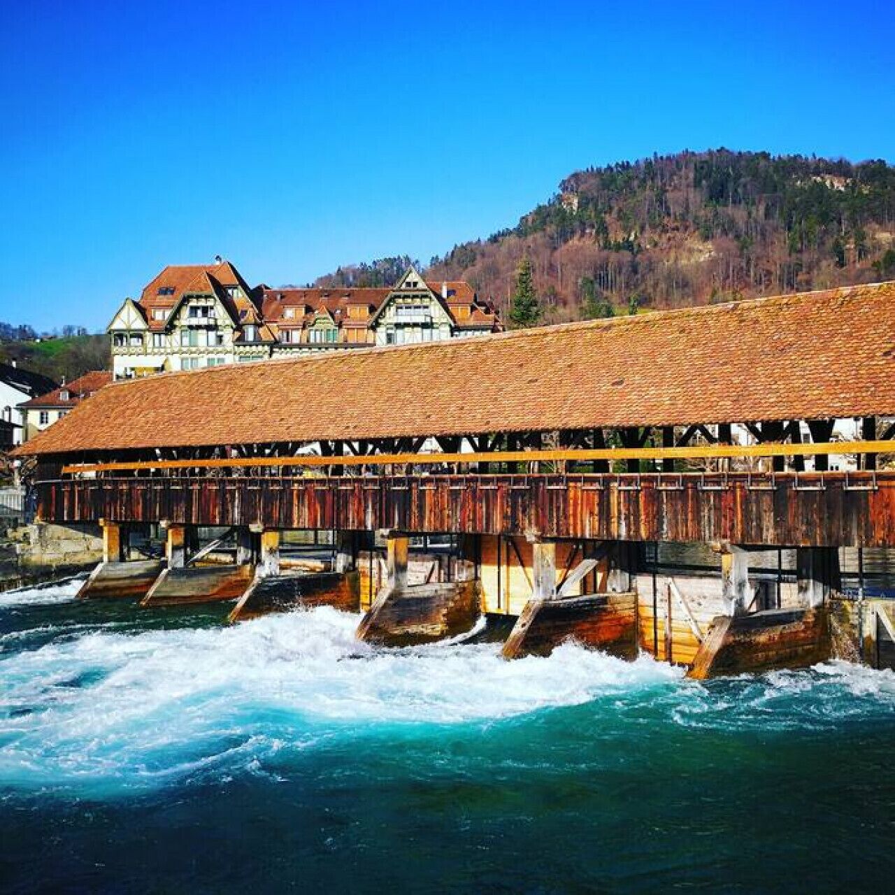 A wooden bridge over a river with a building in the background.