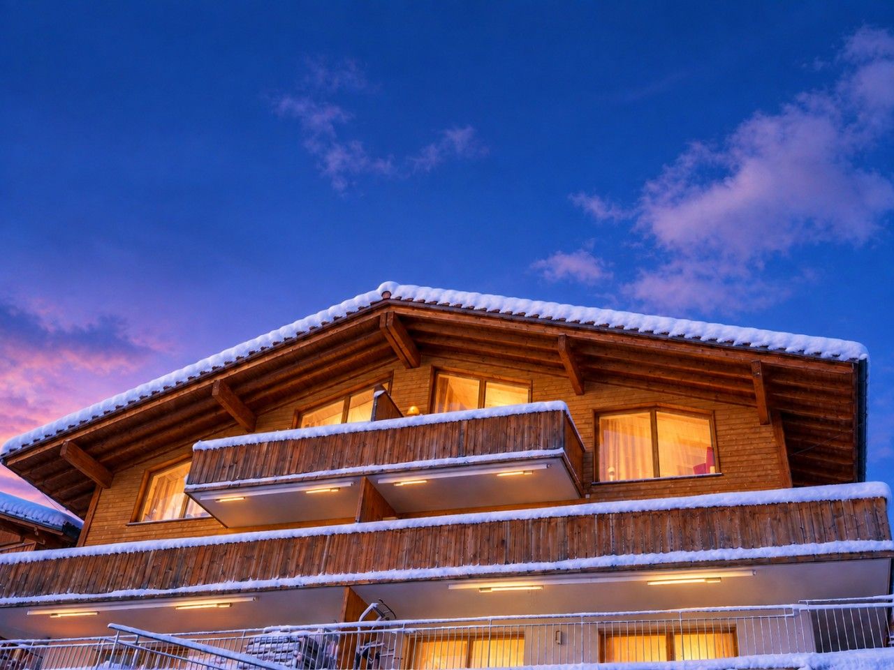Een houten chalet met een balkon en een met sneeuw bedekt dak.