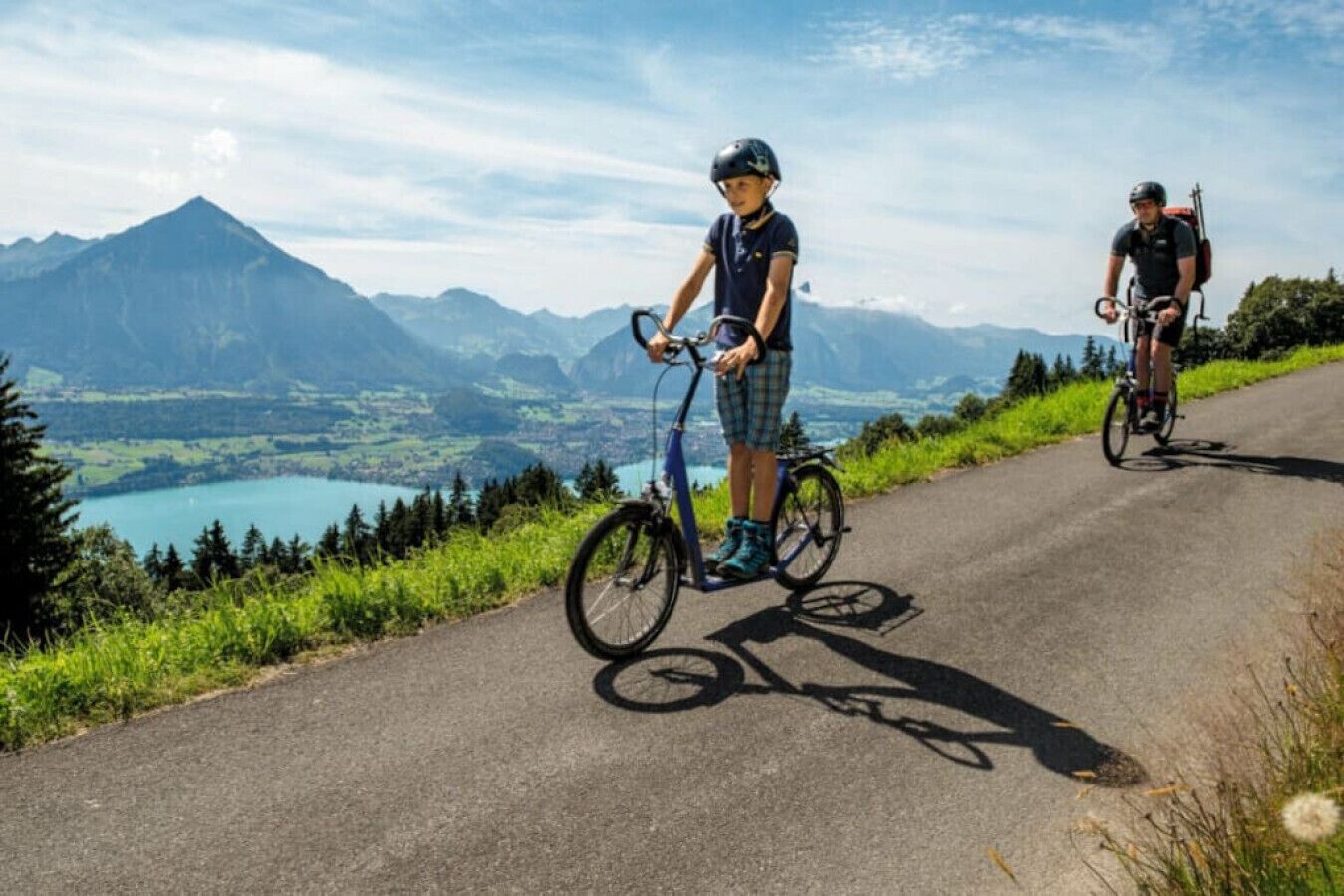 Deux cyclistes sur une piste cyclable, avec une vue panoramique sur les montagnes en arrière-plan.
