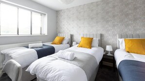 Habitación de hotel con tres camas, ropa de cama blanca y un papel tapiz estampado.
