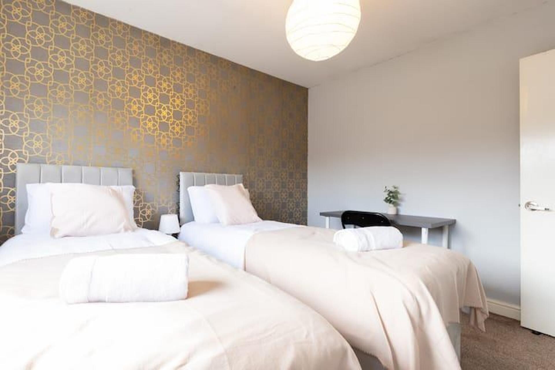 Una habitación de hotel con dos camas, un escritorio y un papel tapiz estampado.