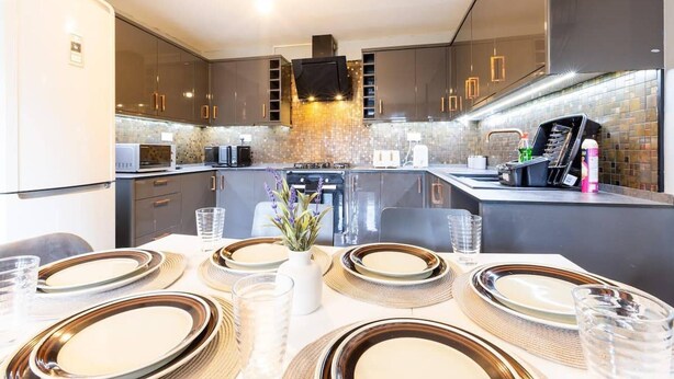 Una cocina moderna con armarios oscuros, una isla central y un comedor para cuatro personas, con platos y vasos.