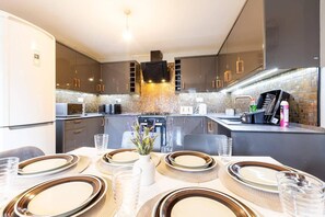 Una cocina moderna con armarios oscuros, una isla central y un comedor para cuatro personas, con platos y vasos.