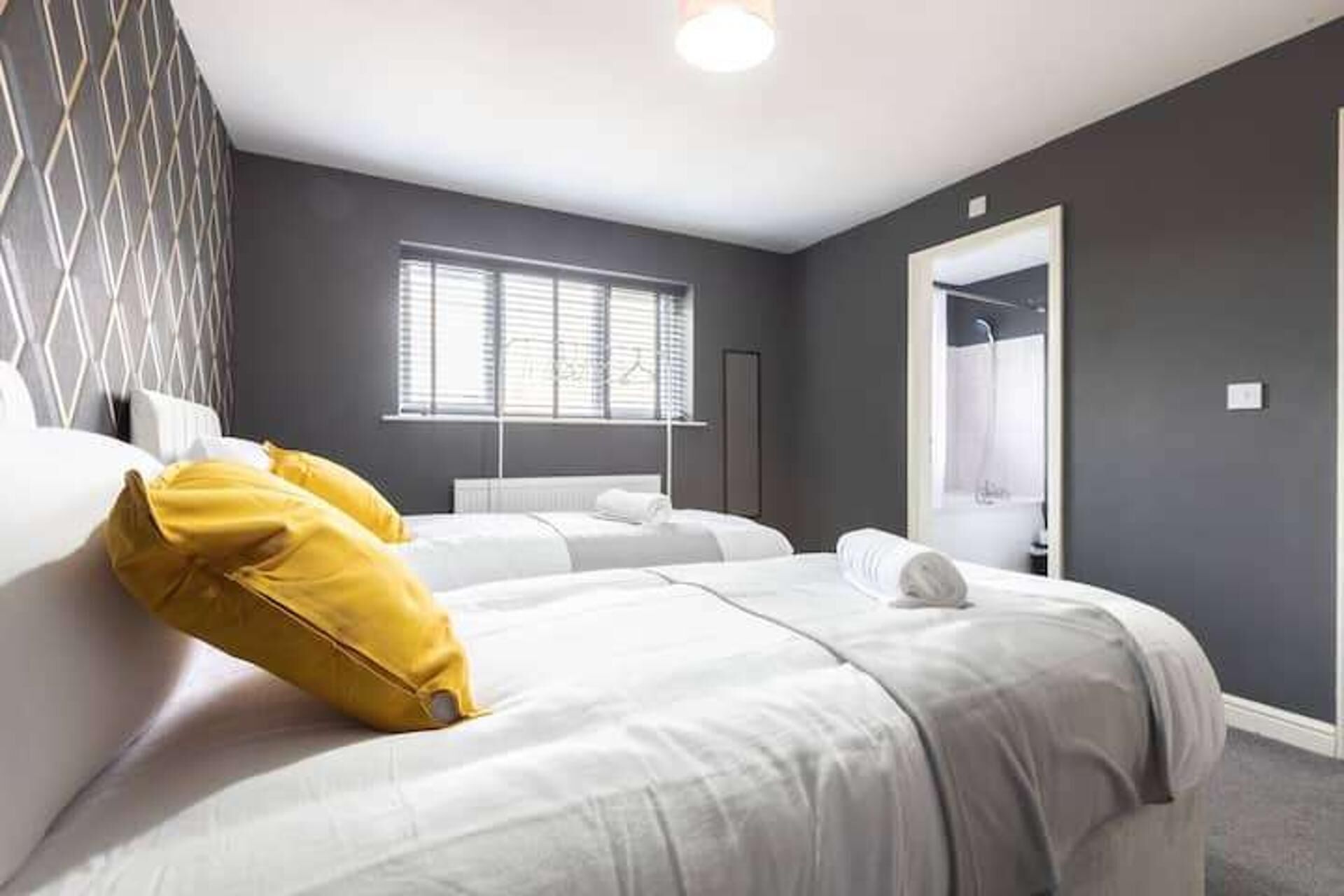 A hotel room with two beds, a window with blinds, a mirror, and a door leading to a bathroom.