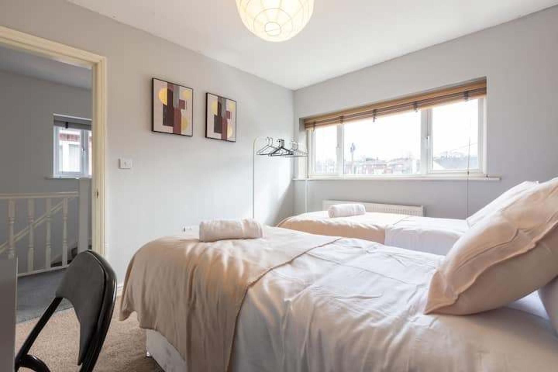 A bedroom with two beds, a window with a view, and a coat rack.