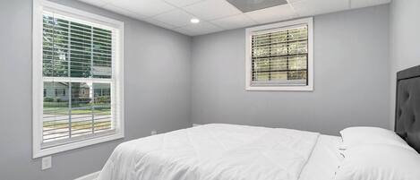 Un dormitorio con una cama, dos ventanas y una lámpara en el techo.