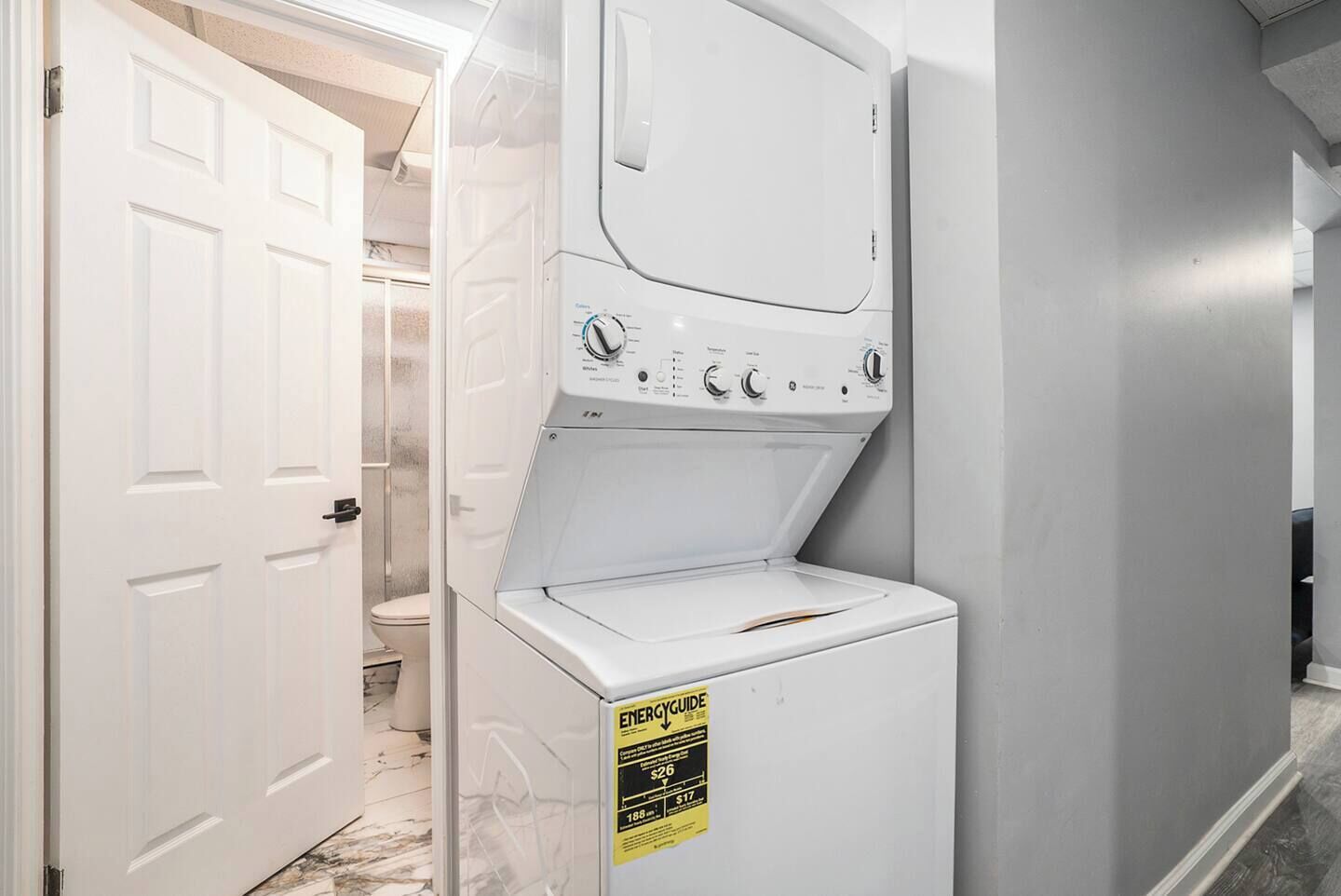 Un lavadero con lavadora y secadora de carga frontal, una puerta que da a un baño y una etiqueta de eficiencia energética amarilla en la secadora.