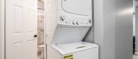 Un lavadero con lavadora y secadora de carga frontal, una puerta que da a un baño y una etiqueta de eficiencia energética amarilla en la secadora.