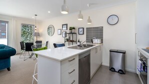 A modern kitchen with white cabinetry, stainless steel appliances, pendant lighting, and a visible trash bin. - Cosy 2BR Close to Light Rail (Harrison)