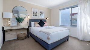 A bedroom with a bed, bedside table, lamp, and artwork on the wall. - Cosy 2BR Close to Light Rail (Harrison)