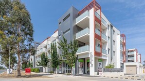 A multi-story residential building with balconies, a garage, and a clear sky. - Cosy 2BR Close to Light Rail (Harrison)