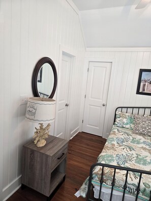 A bedroom with a bed, a nightstand with a lamp, a mirror, and a door. - Charming carriage house in marvelous Watercolor. (Santa Rosa Beach)