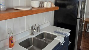 Eine Küche mit weißen Schränken, einer doppelten Spüle, einem schwarzen Kühlschrank und Holzregalen mit verschiedenen Küchenutensilien.