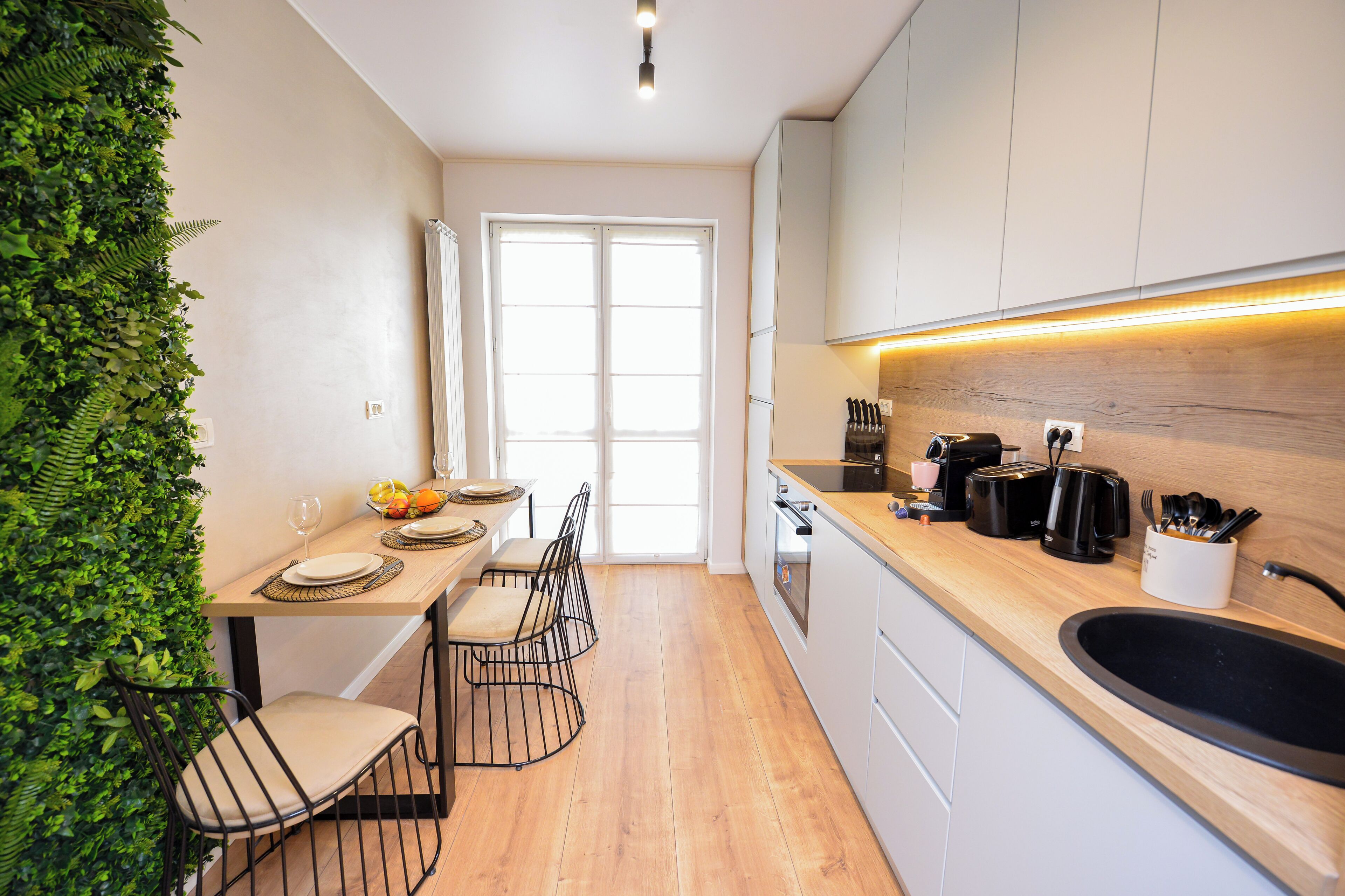 A modern kitchen with a wooden countertop, a sink, and a dining area with two chairs and a table set for two.